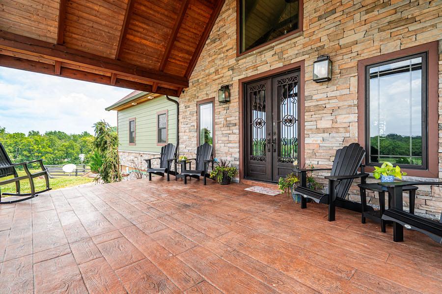 Photo of large outdoor living space at front of log home with stone facade. The porch is exposed a-framed wood and a stone flooring