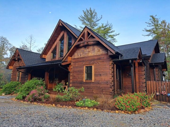 photo of log home with flat log facade. The home has a cottage appearance with geometric windows over the covered porch at the front door.