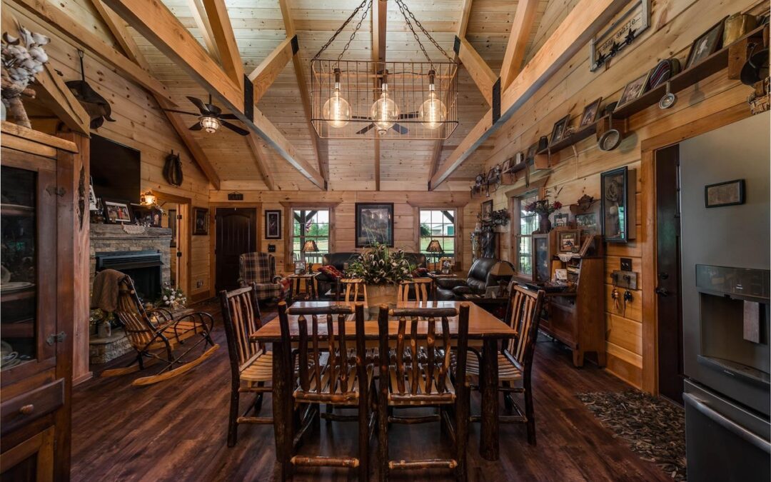 Photo of log home dining room and living space with wood ceiling and a-framed. supports. Dark wood floors and exposed wood walls