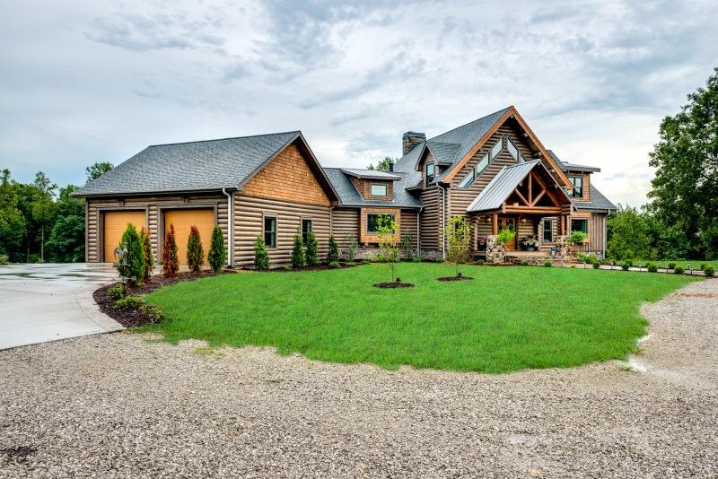 Photo of round log facade log home. Front entrance has geometric windows above a-frame covered entrance.