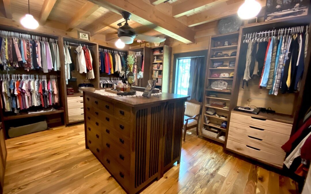 Photo of a his and her's master bedroom closet with wood floors, exposed wood ceilings and support beams, middle wood island and clothes racks, drawers and shelves